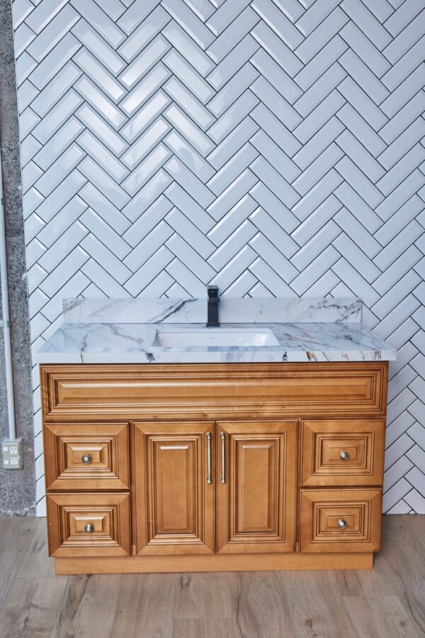 Wooden bathroom vanity with marble countertop against herringbone tile wall.