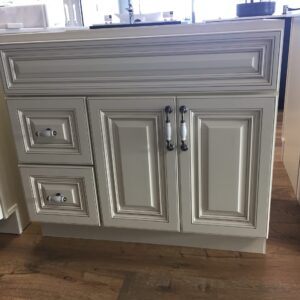 White kitchen cabinet with ornate paneling and silver handles on wooden floor.