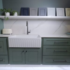 Modern kitchen with green cabinets, white sink, and decorative frames on shelf.